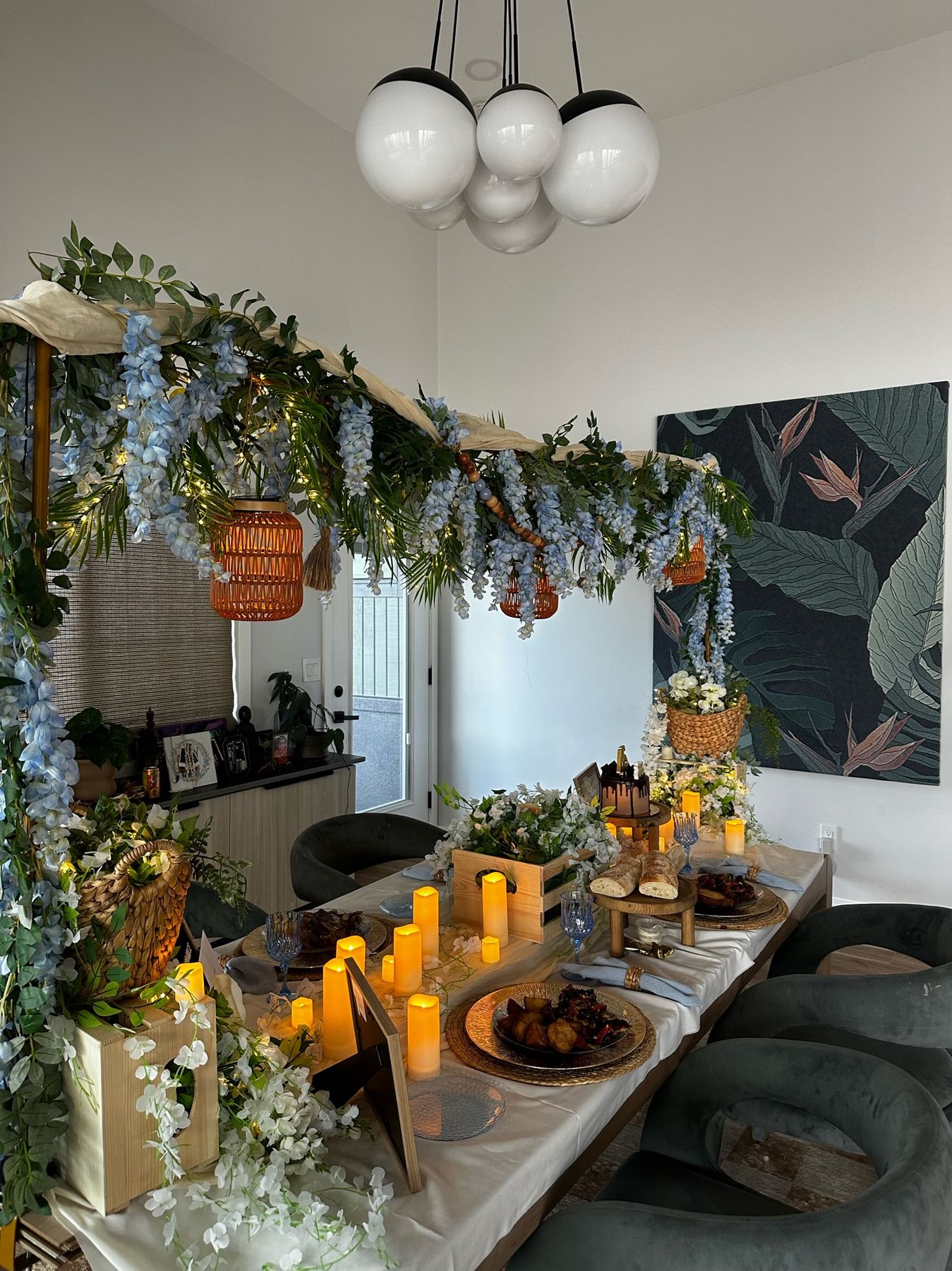 Long candlelit dinner table set with blue glassware and woven chargers