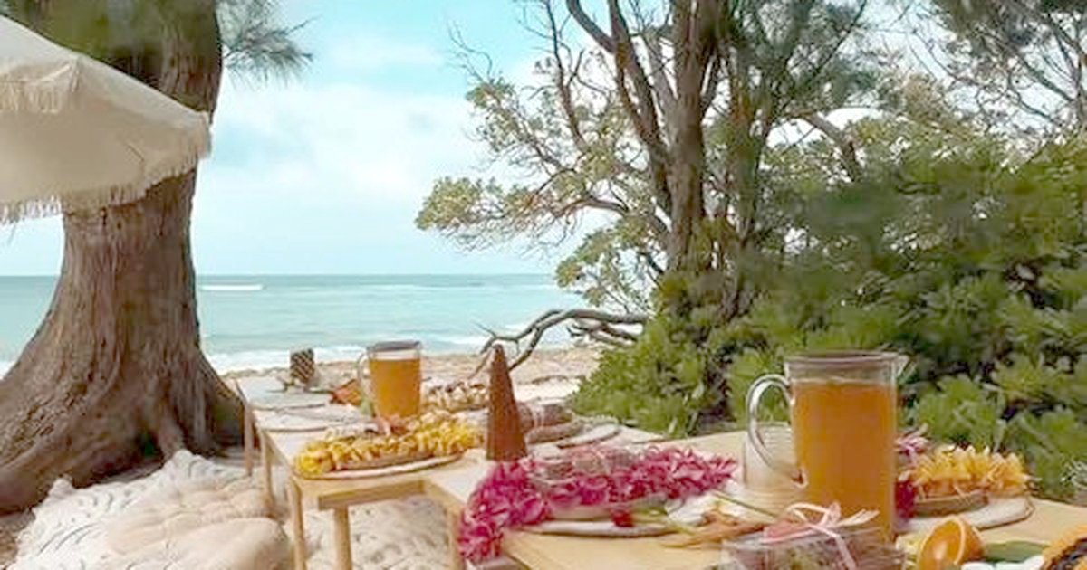 Pitchers of juice and grazing boards on low wooden tables beside the ocean