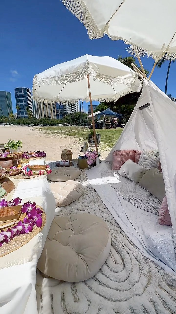 Fringed umbrellas and a teepee lounge at Ala Moana Beach Park with the skyline behind