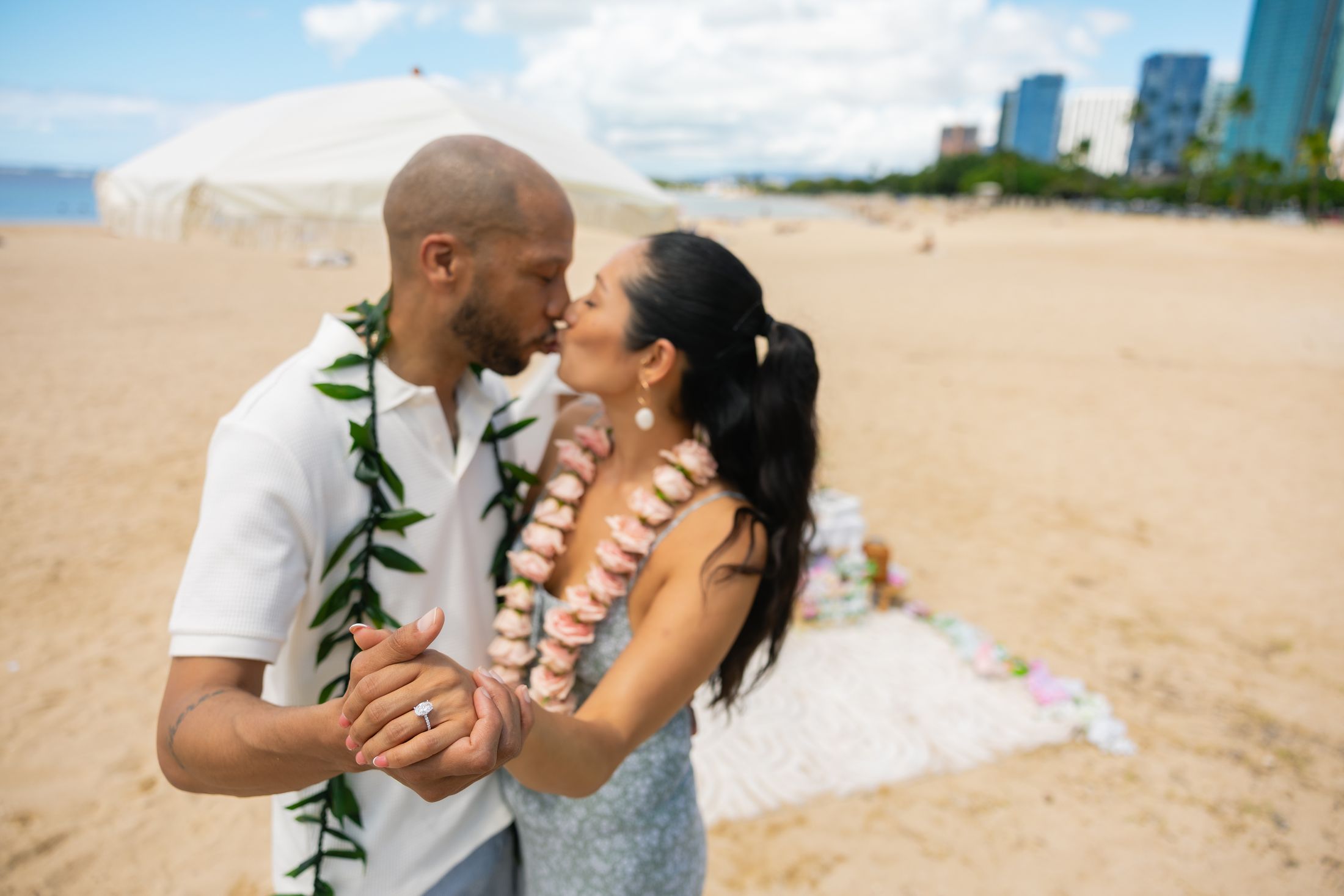 Emily and James kiss on the beach in flower and maile leis