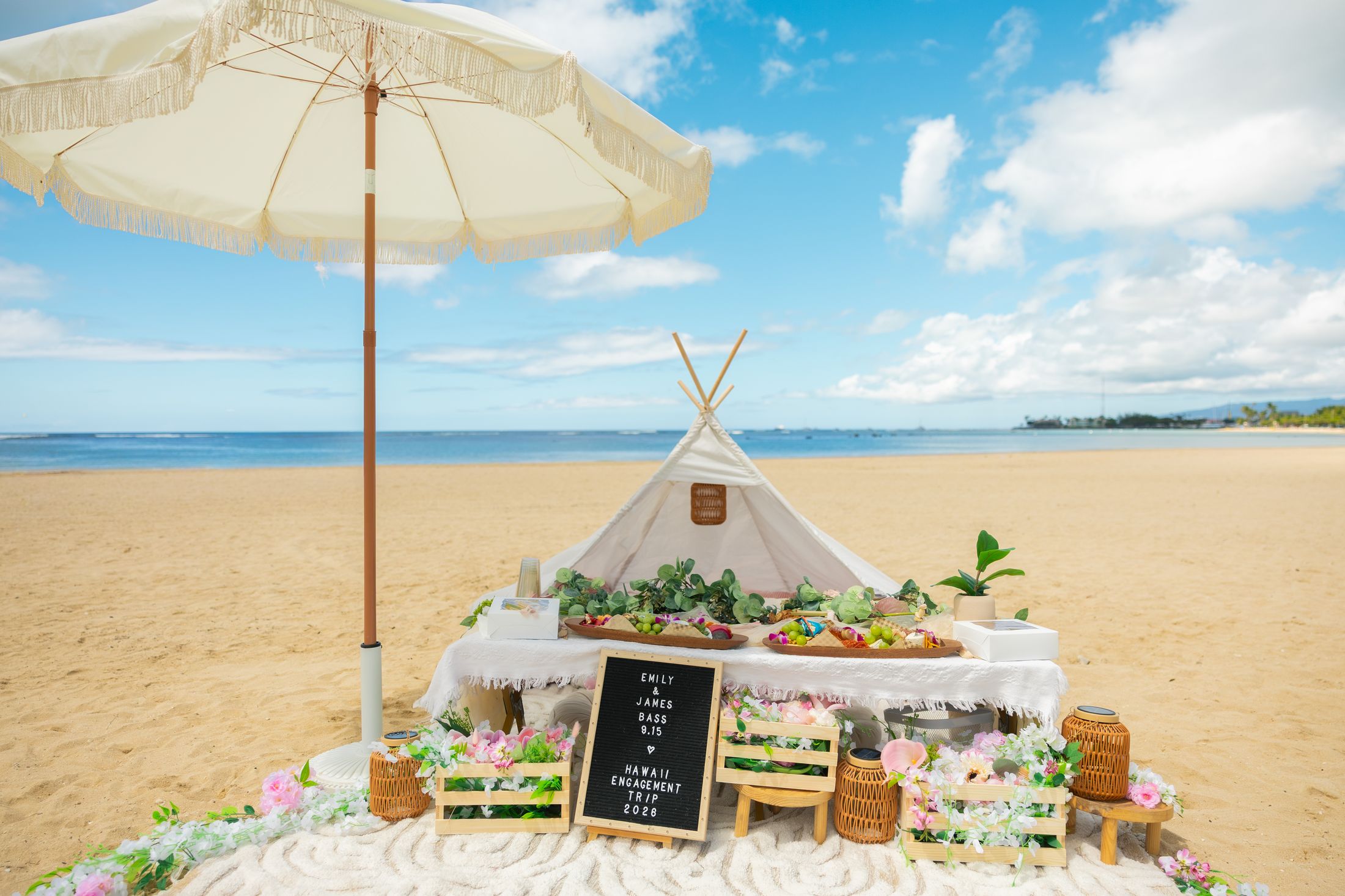 Full beach picnic setup with fringed umbrella, teepee and floral crates