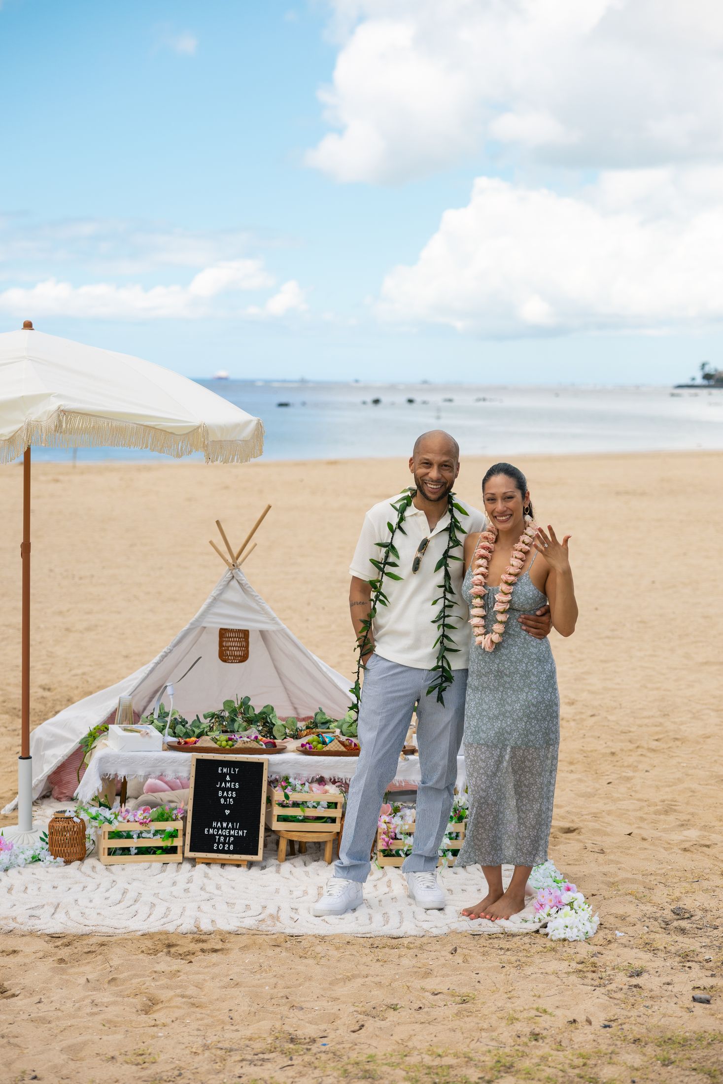 Emily and James in flower leis in front of their teepee picnic