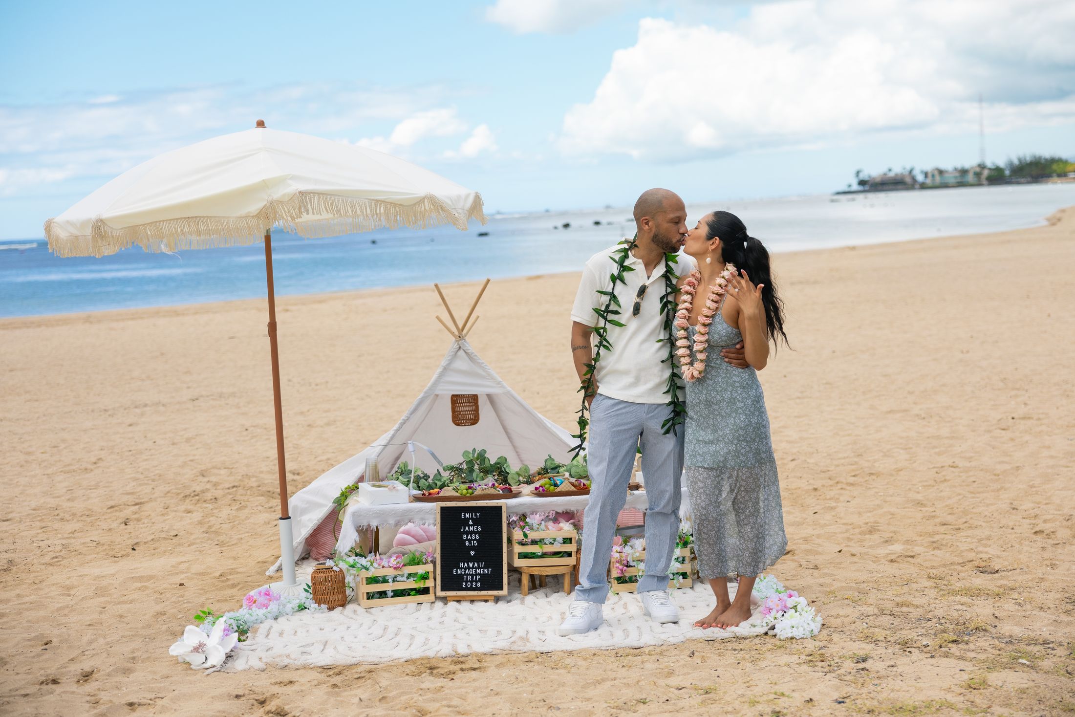 Emily and James kiss beside their beach picnic setup