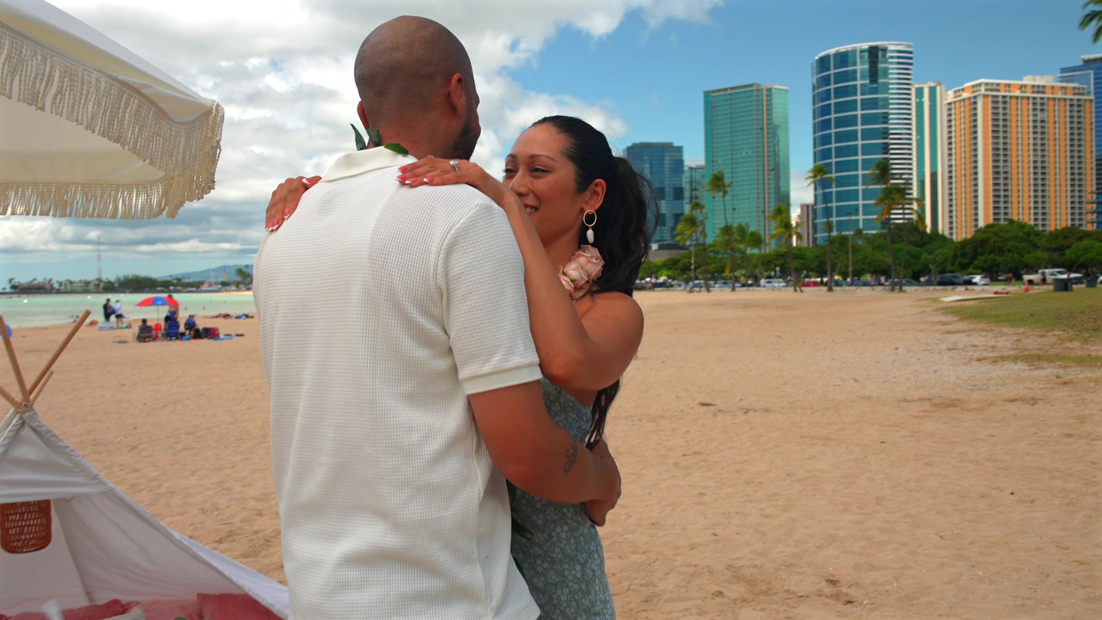 Emily and James embrace with the Honolulu skyline behind them