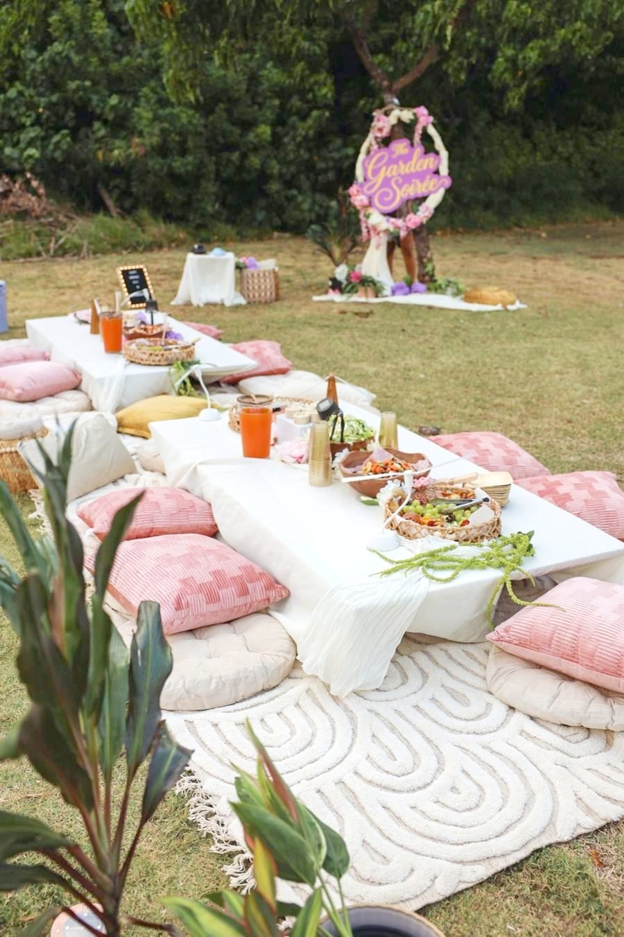 The Garden Soirée lawn party with low white tables, blush pillows and a floral hoop sign