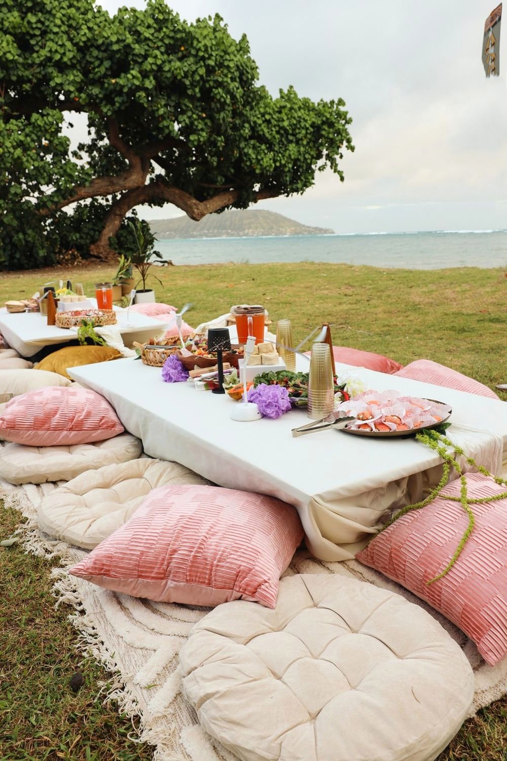 Low white table with blush pillows on a carved rug by the ocean