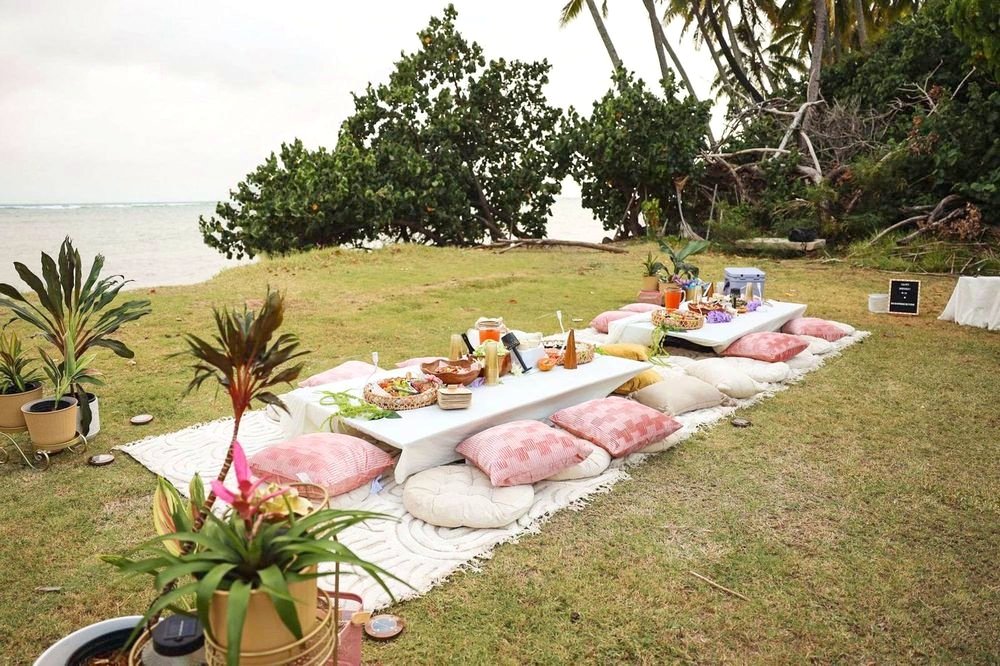 Long row of low white tables and blush cushions on an oceanfront lawn